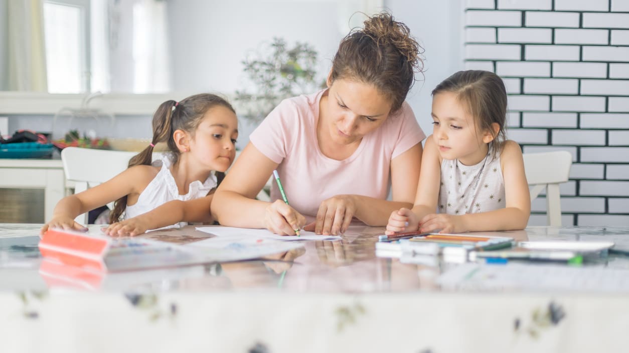 A mother and her two daughters are sitting at a table doing homework.
