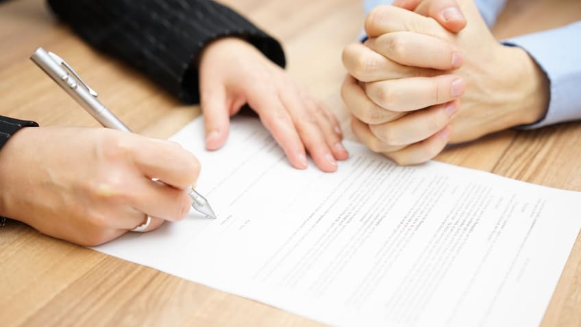 Two people signing a contract on a table.
