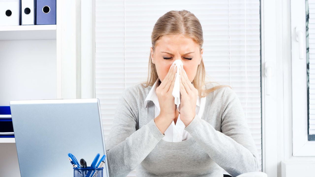 A woman is sneezing at her desk.