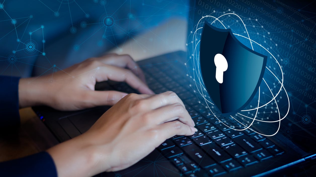 A person typing on a laptop with a shield on it.