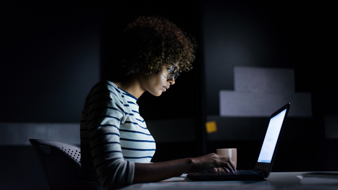 A woman working on a laptop in a dark room.