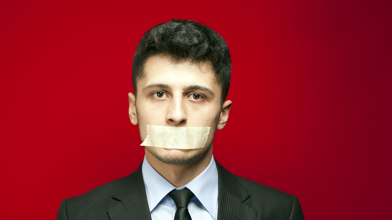 A man in a suit with a piece of tape on his mouth.