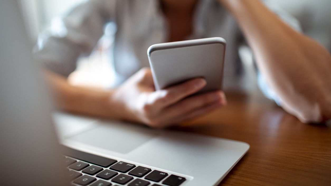 A woman is using a cell phone in front of a laptop.