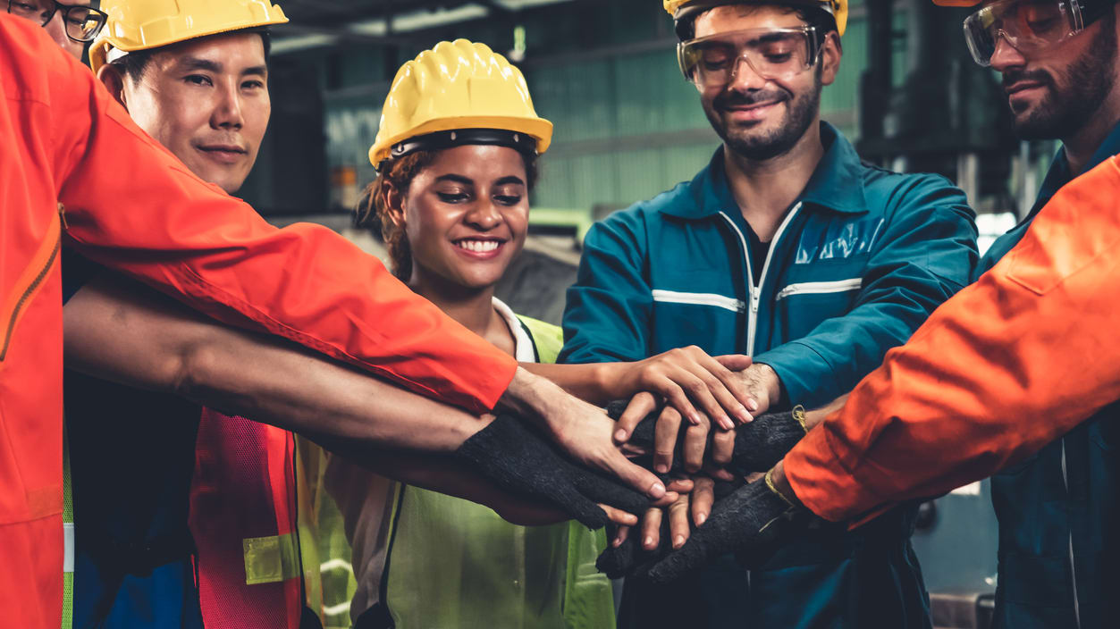 A group of workers putting their hands together in a factory.