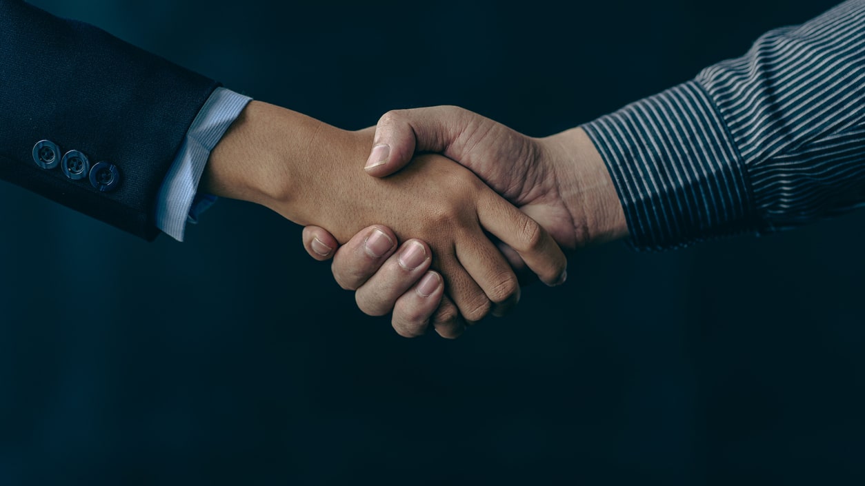 Two business people shaking hands over a dark background.