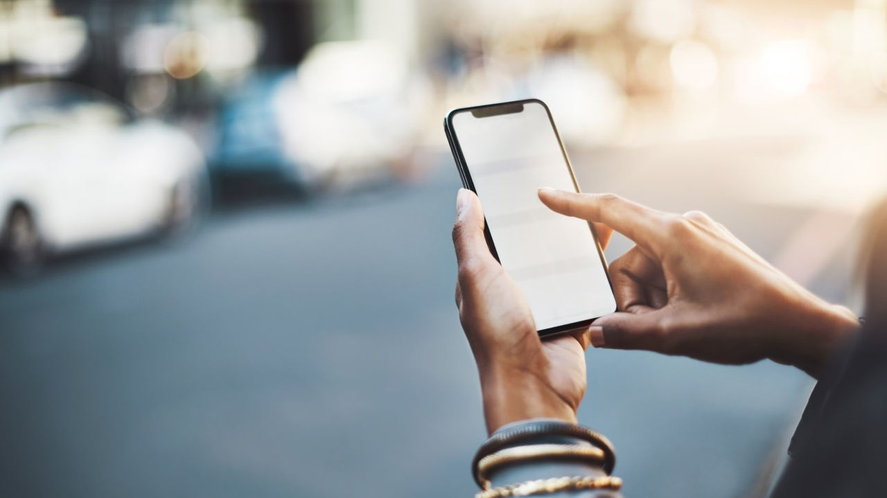 A woman's hand holding a smartphone in front of a street.