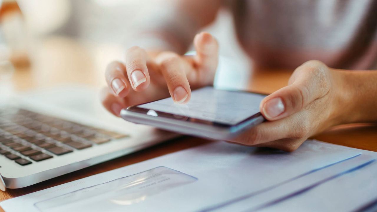 A woman's hand holding a cell phone next to a laptop.