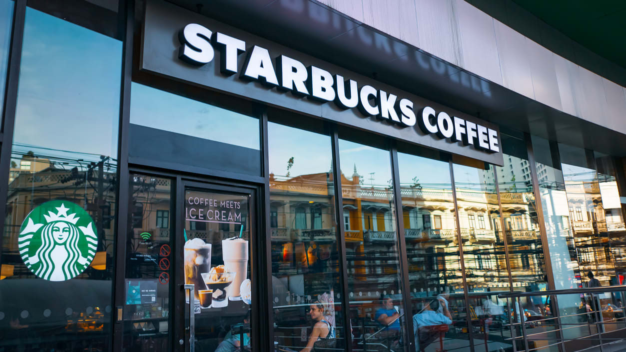 A starbucks coffee shop with people walking in front of it.