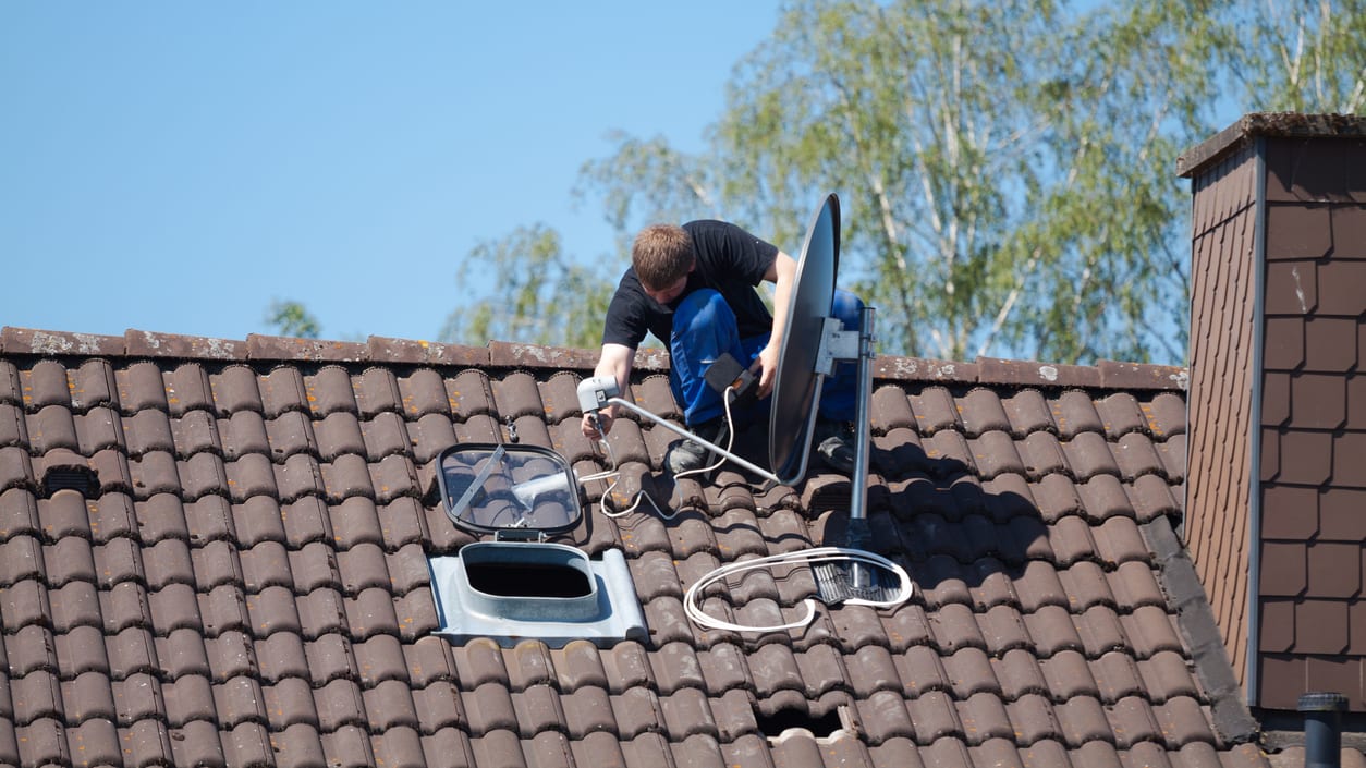 A man installing a satellite dish on a roof.