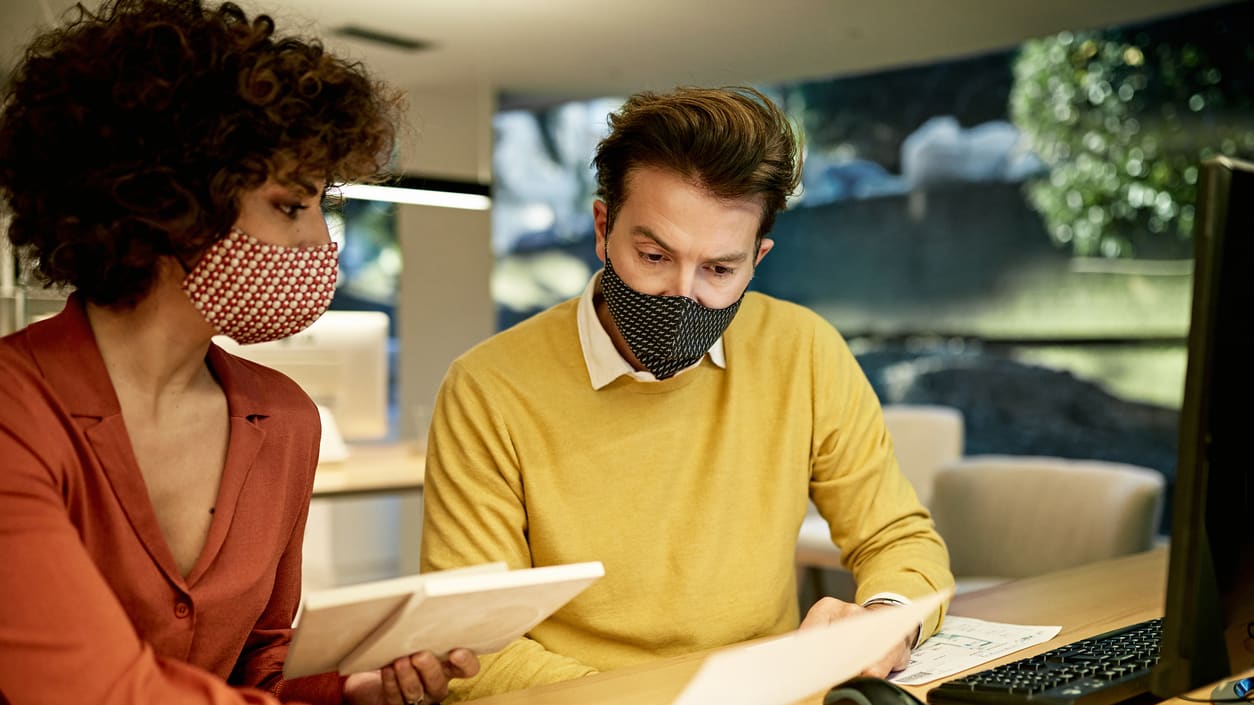 Two people wearing face masks at a desk.