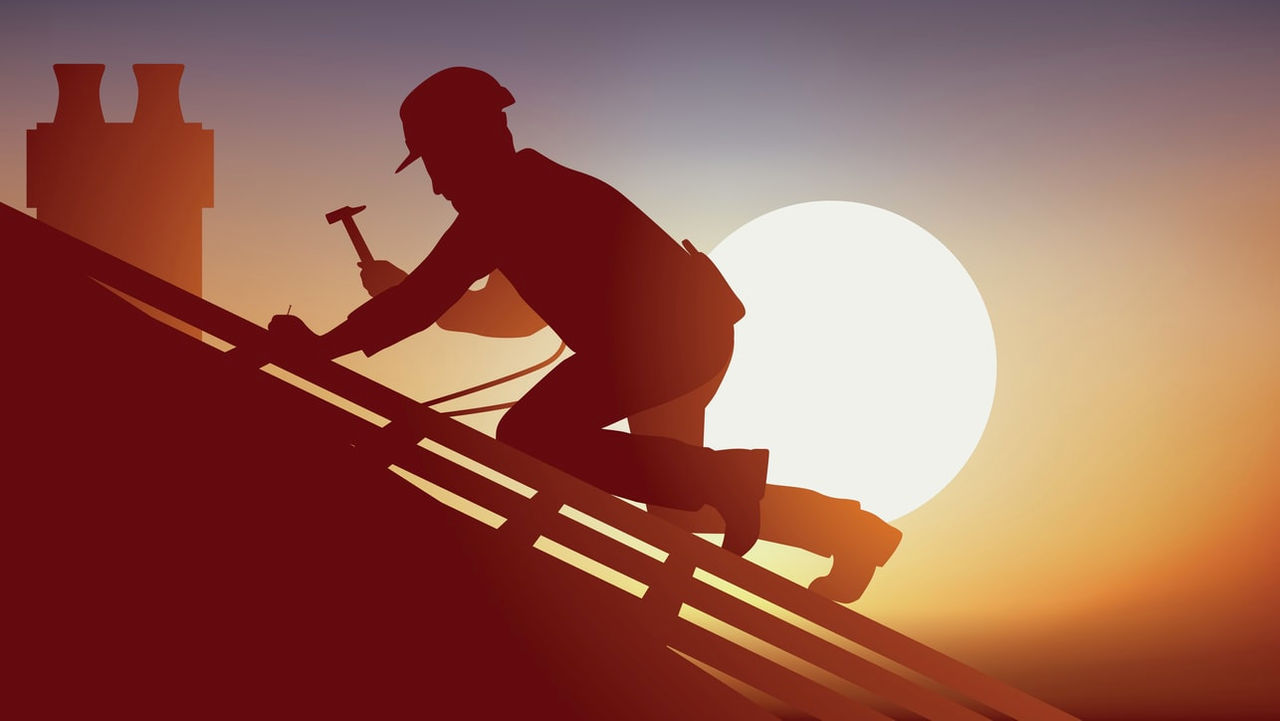 A silhouette of a man working on a roof at sunset.