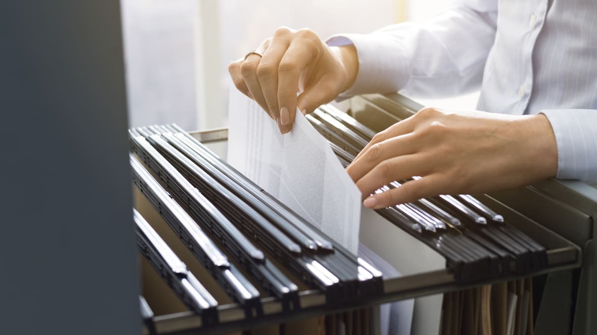 A person is putting papers into a file cabinet.