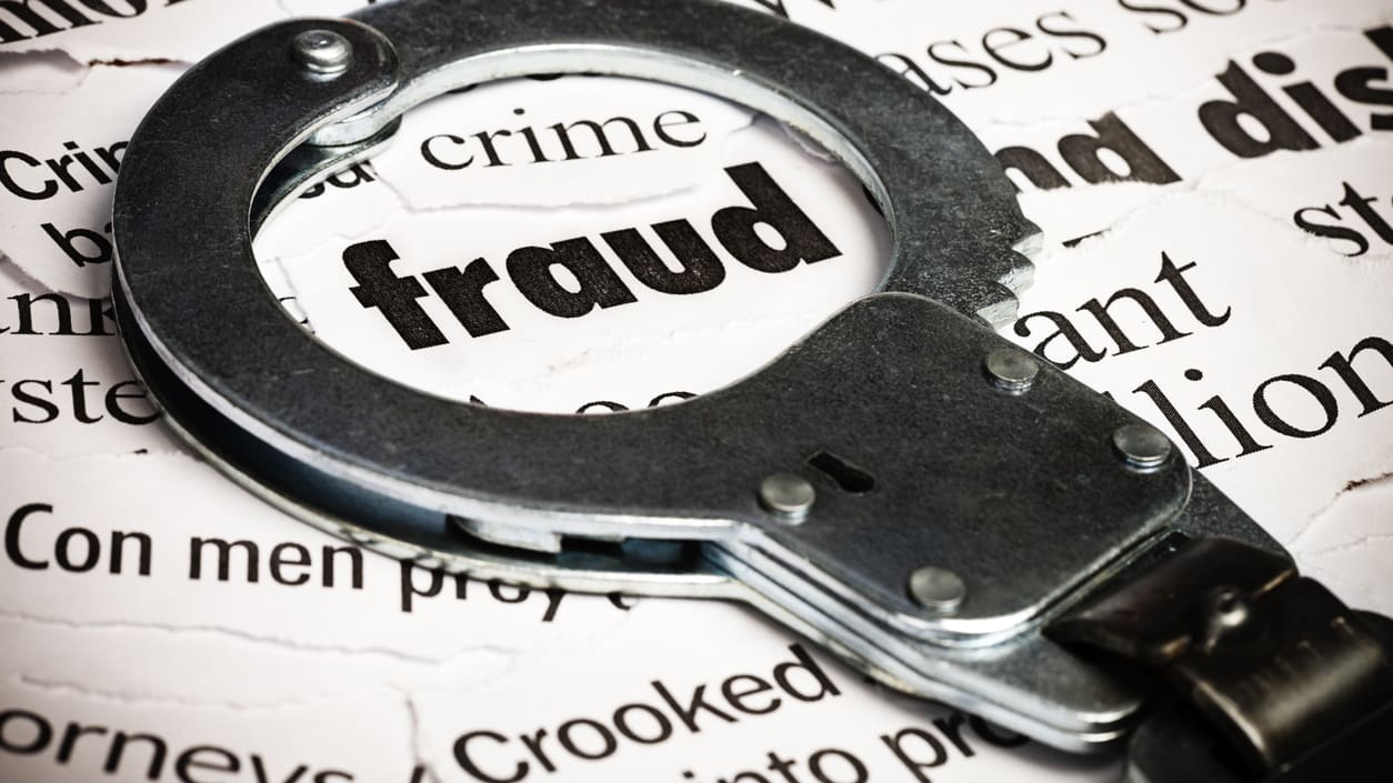 A pair of handcuffs on top of a newspaper with the word fraud.