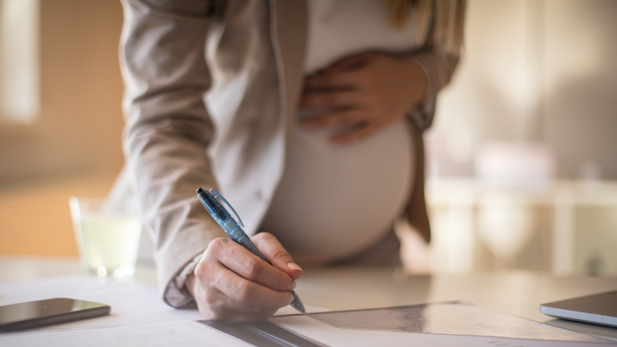 A pregnant woman is writing on a piece of paper.