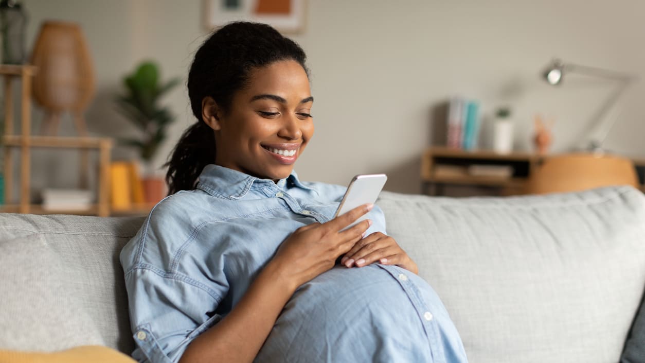 A pregnant woman looking at her phone while sitting on the couch.