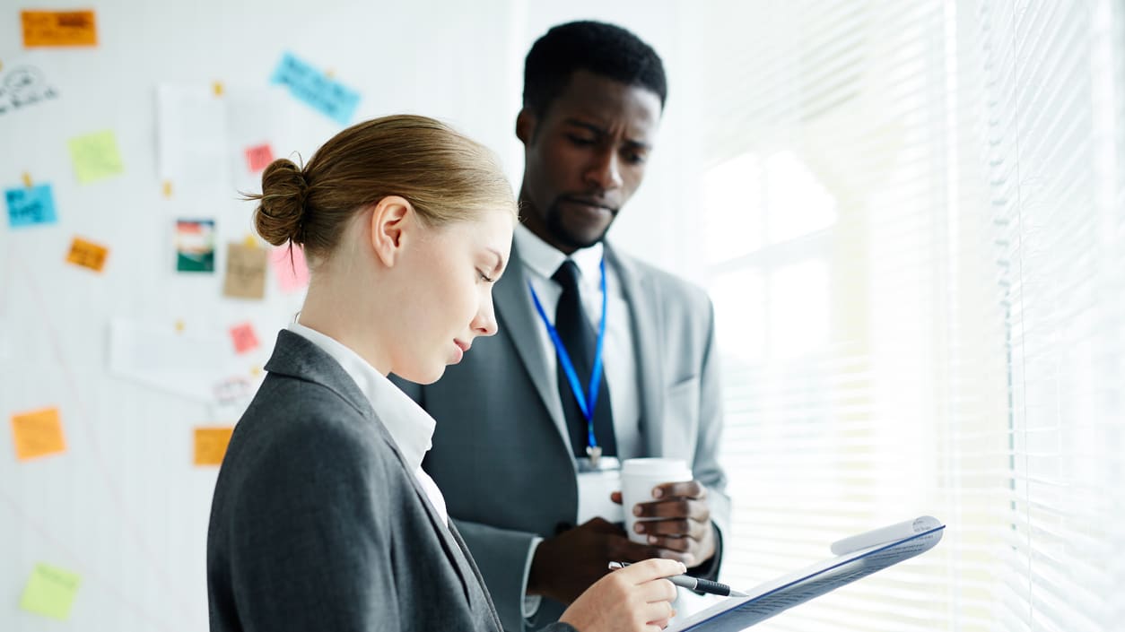 A businessman and woman are looking at a clipboard.
