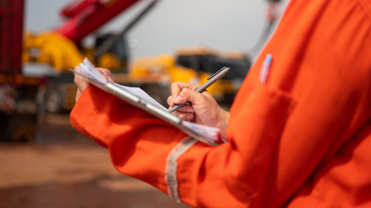 Workplace safety officer making notes on clipboard at construction site