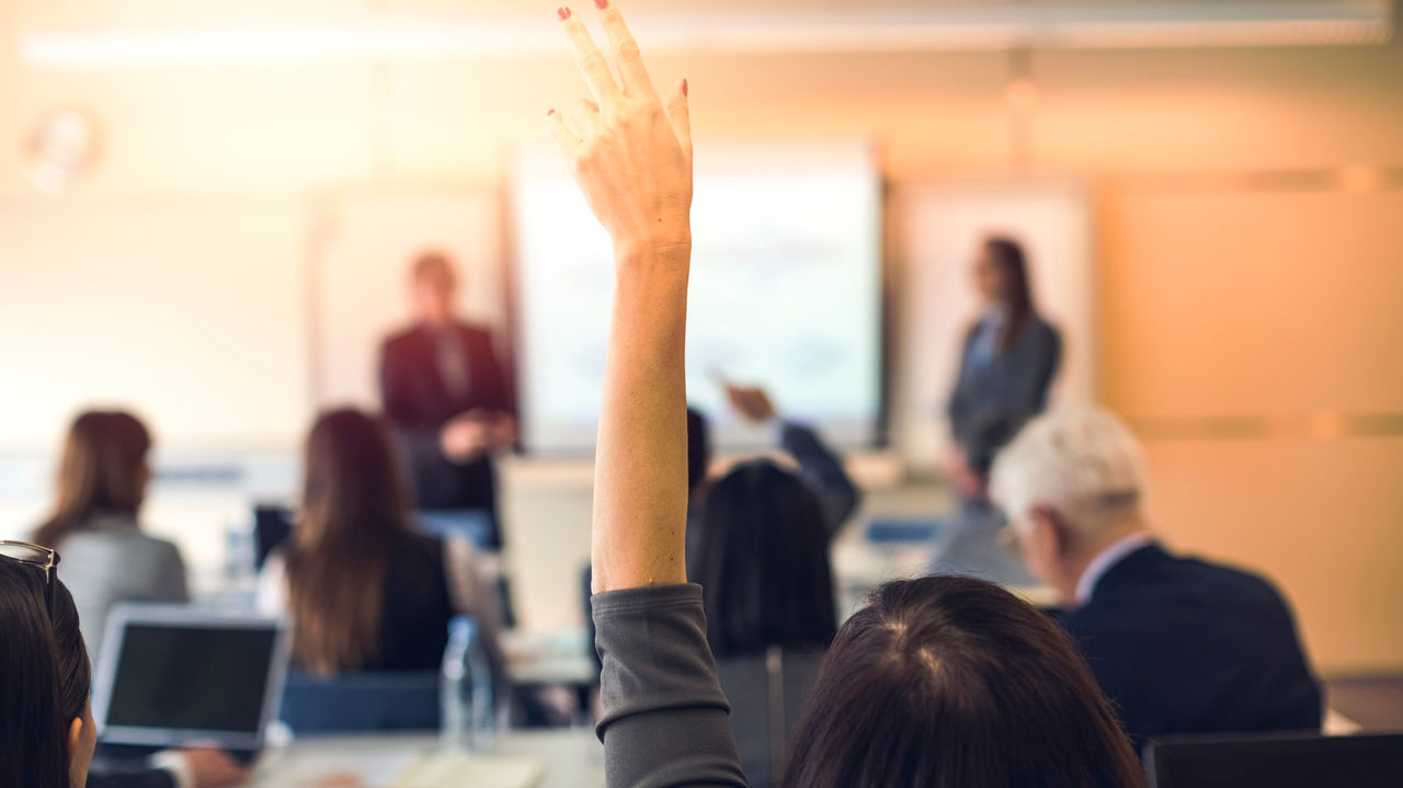 A group of business people raising their hands in a conference room.