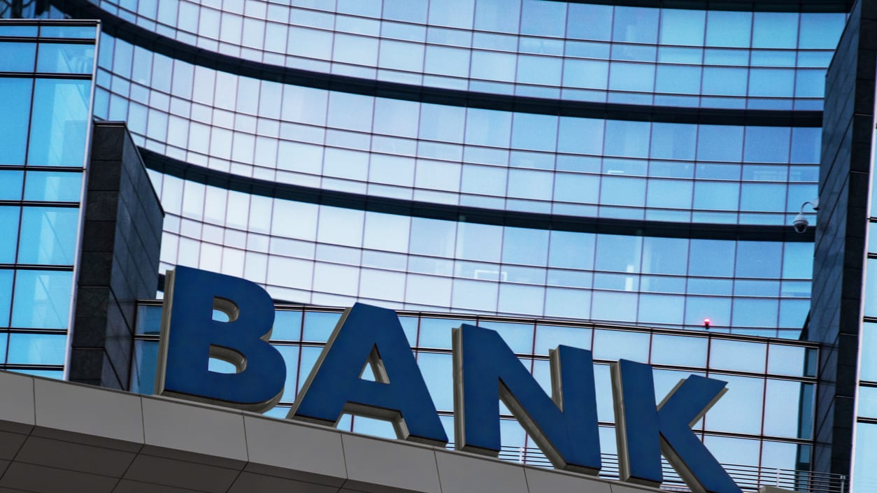 A bank sign is on top of a glass building.