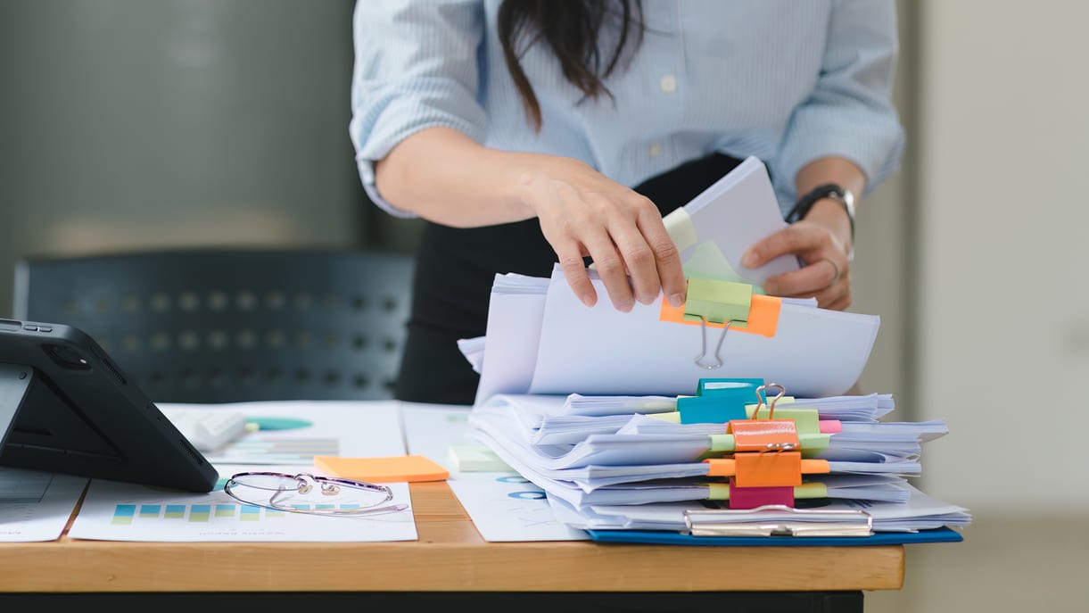 A woman is putting papers on a desk.