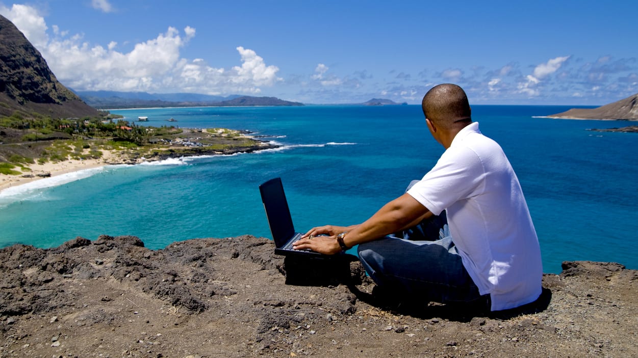 A man sitting on a cliff with a laptop.