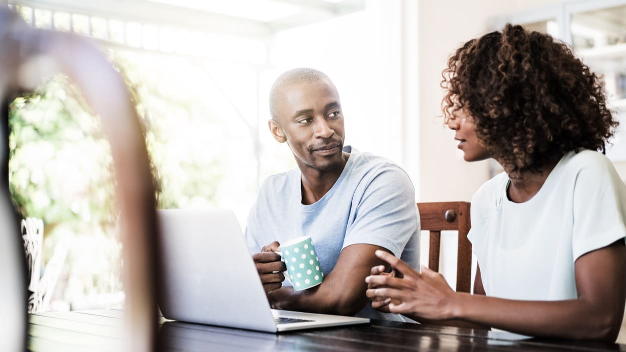 A man and woman sitting at a table looking at a laptop.