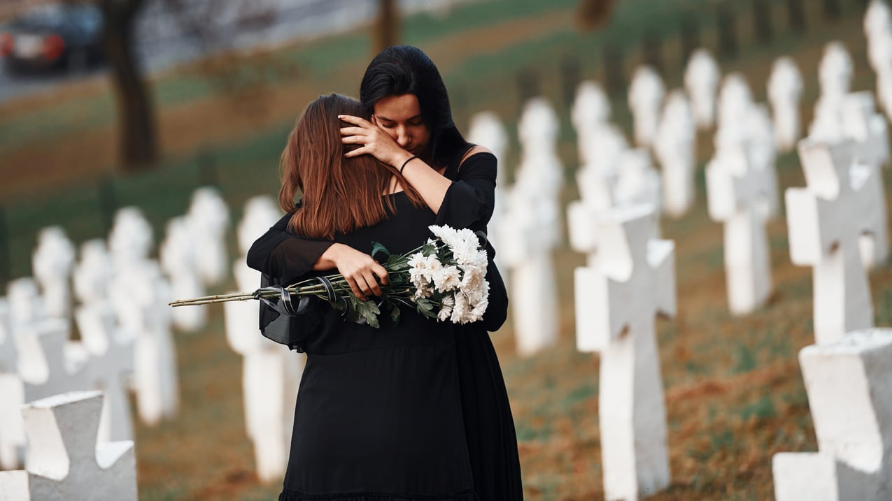 Two women hugging each other in a cemetery.