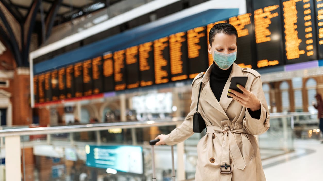 A woman wearing a face mask and carrying a suitcase in a train station.
