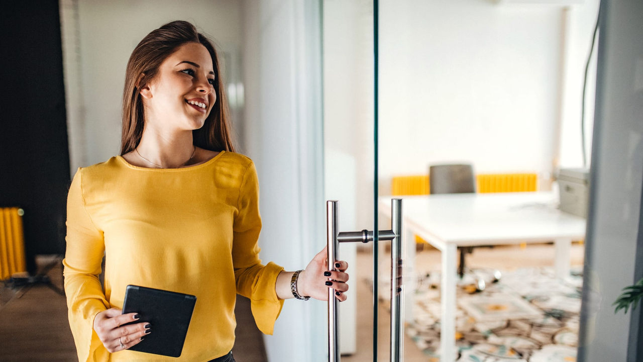 A young woman holding a notebook in front of a glass door in an office.