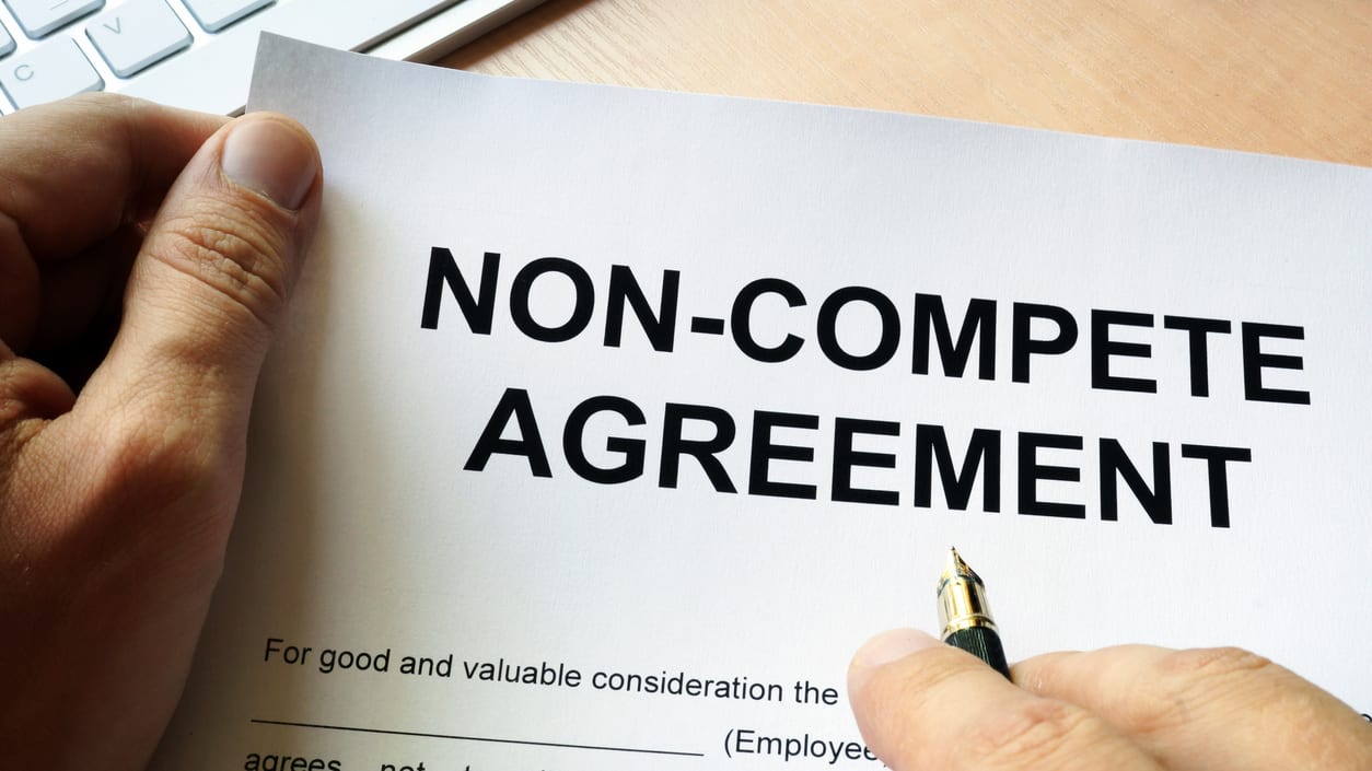 A person signing a non - compete agreement on a desk.