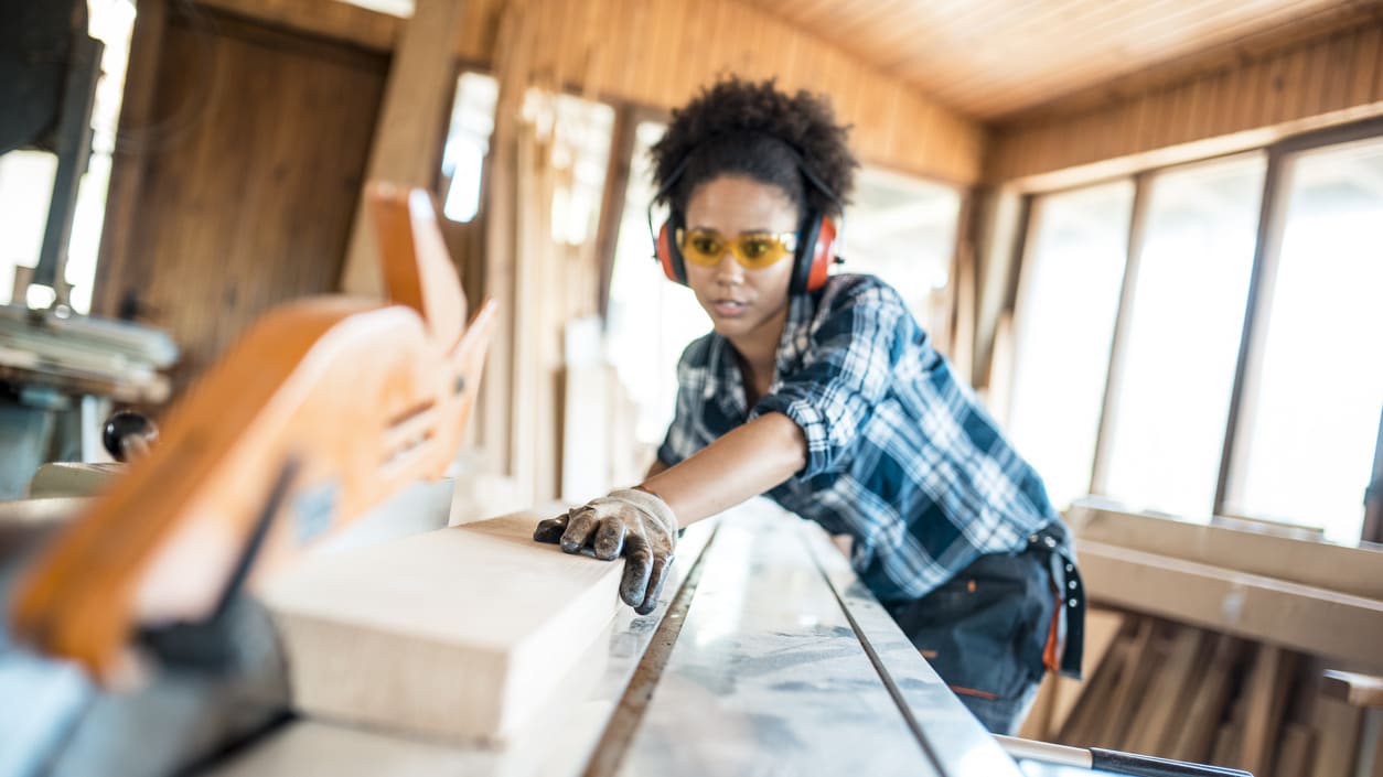 A woman working with a table saw in a wood shop.