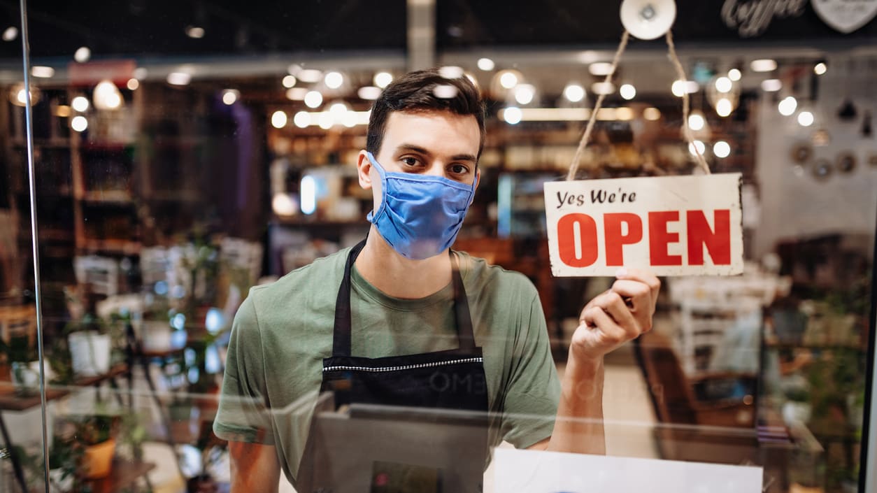 A man wearing a face mask is holding a sign that says open.