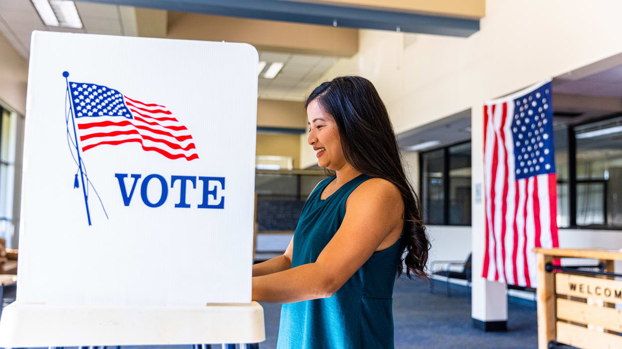 A woman voting in a voting booth with an american flag.