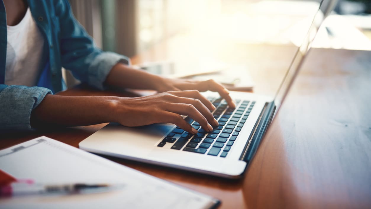 A woman typing on a laptop in front of a window.