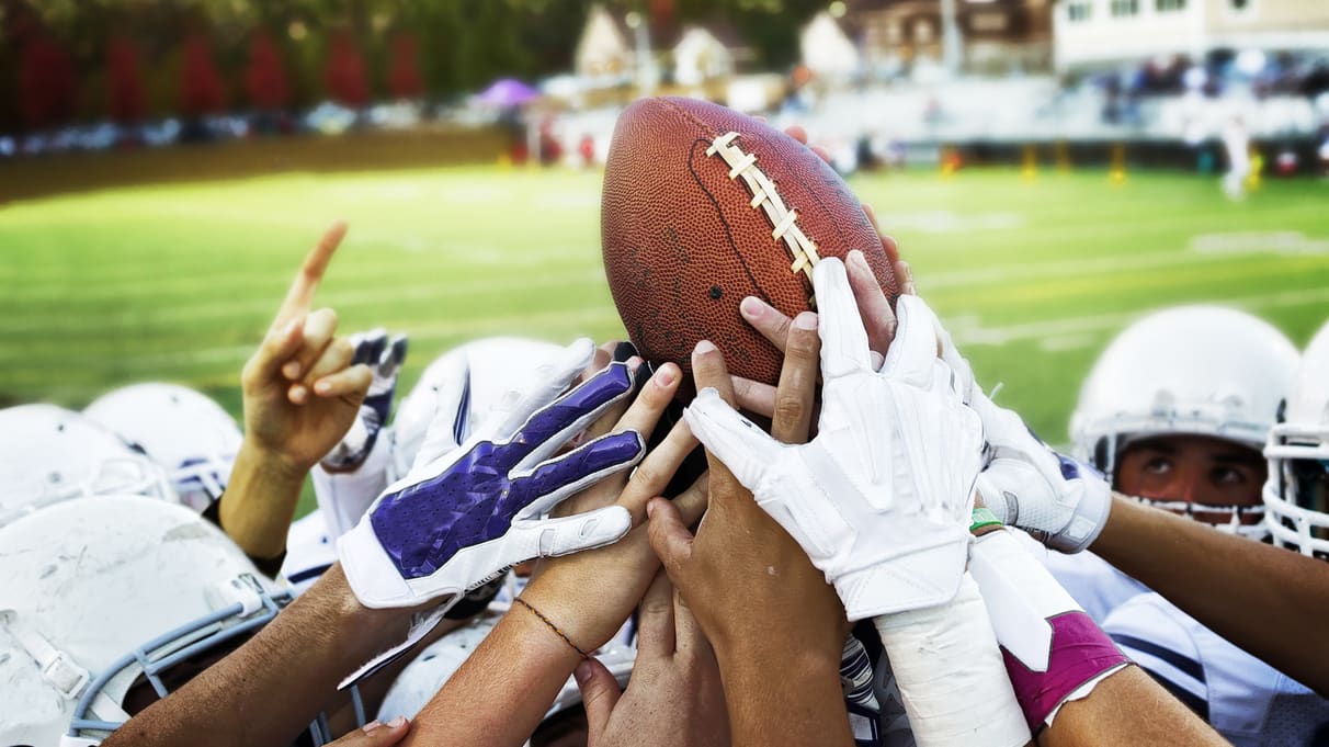 A group of football players huddle around a football.