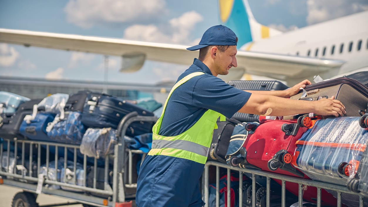 A man loading luggage onto a cart at an airport.