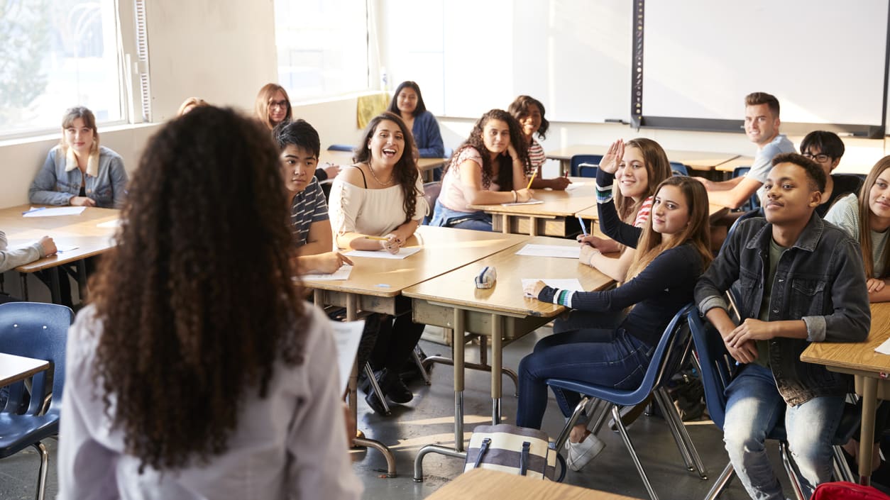 A group of students in a classroom listening to a teacher.