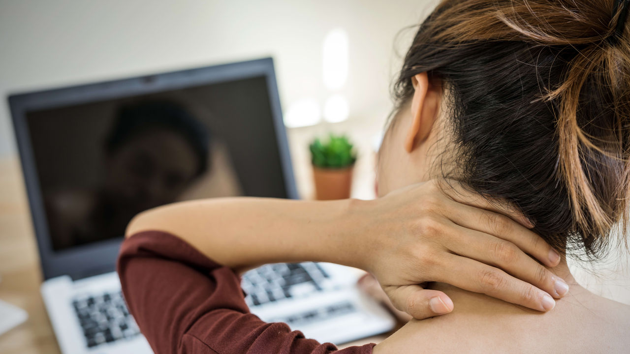 A woman is holding her neck in front of her laptop.