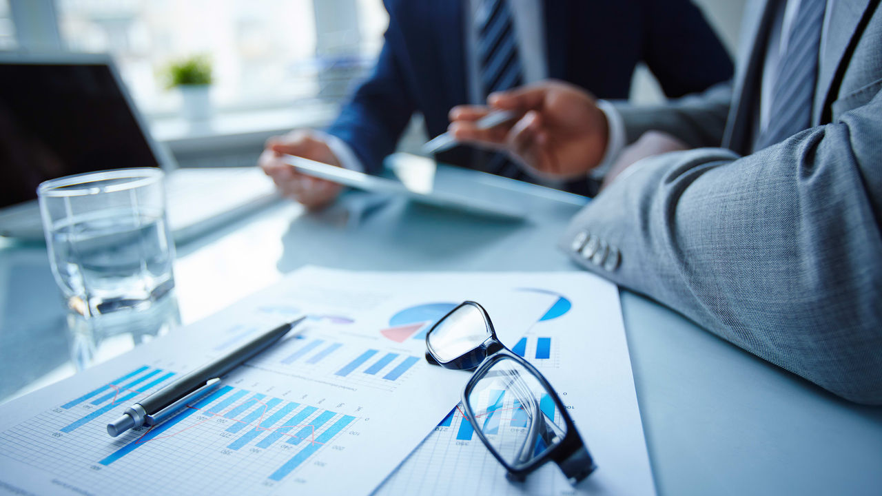 Two business people sitting at a table with papers and graphs.