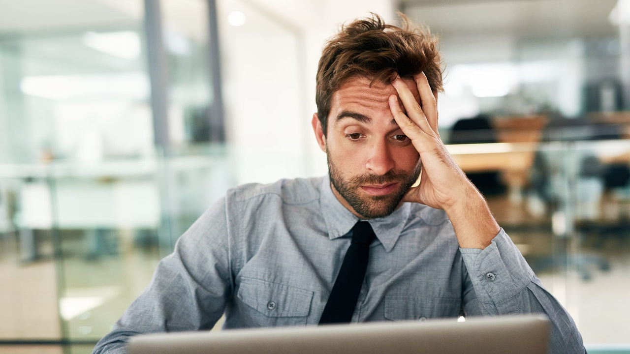 A man with his hand on his head looking at his laptop.