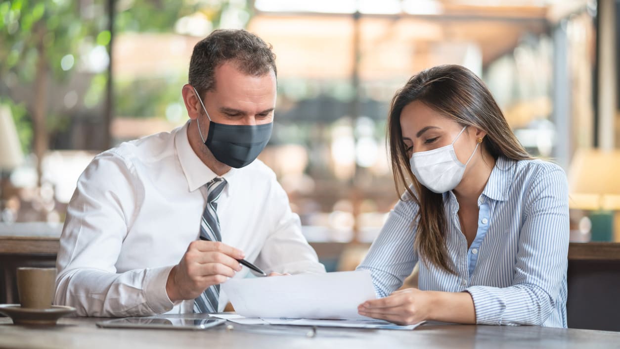 A man and woman wearing a face mask are sitting at a table.