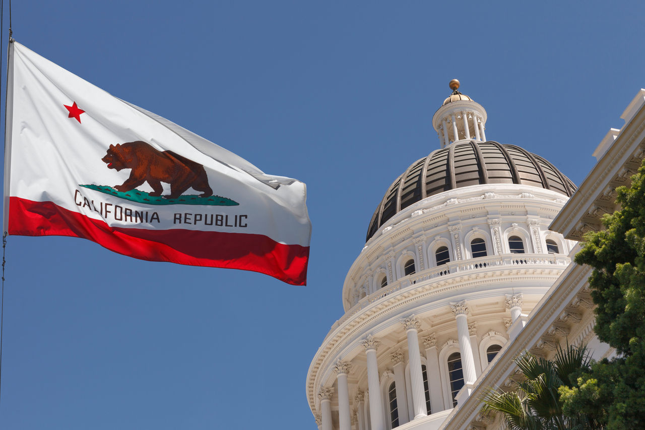 The California state capitol with the state flag waving before it.