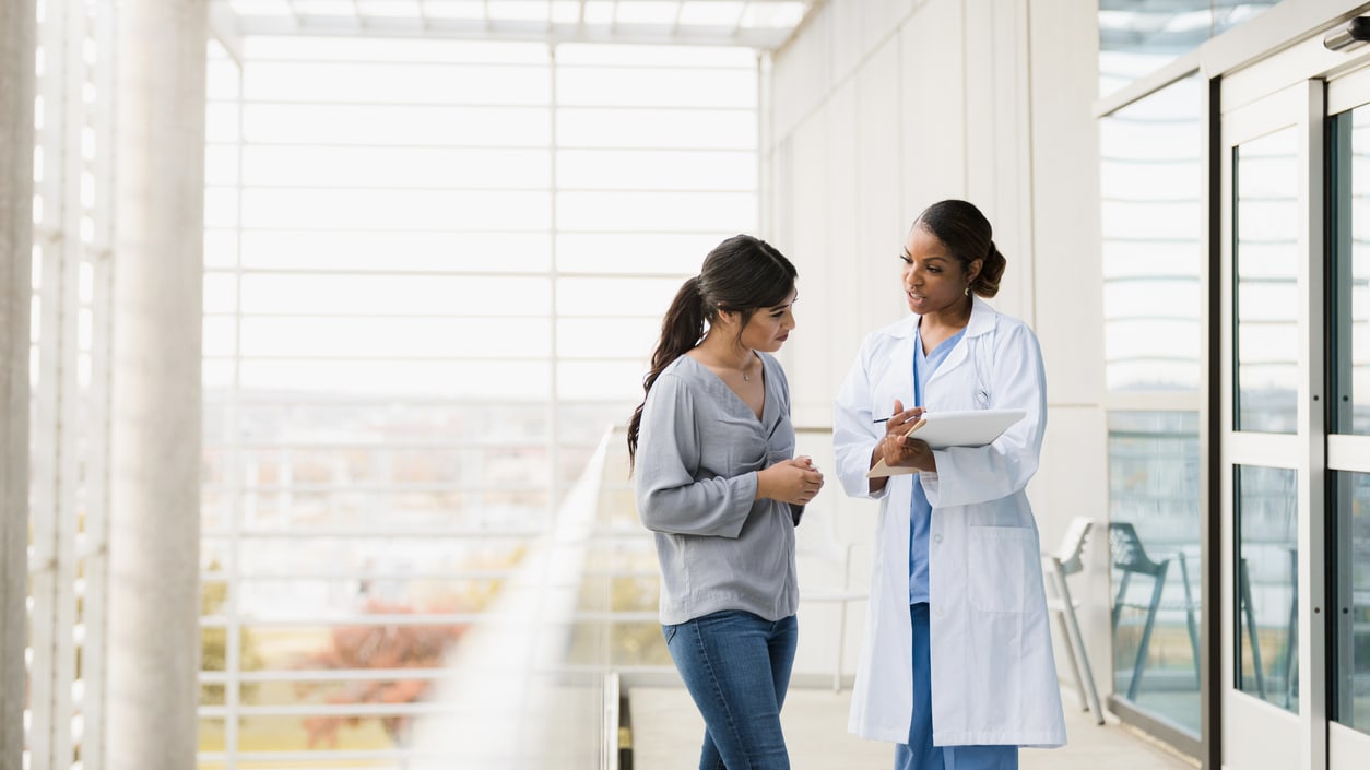 Two female doctors talking on a walkway in a hospital.