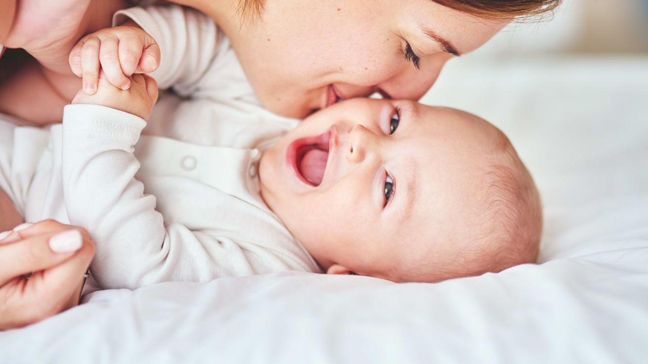 A woman kissing her baby on the bed.