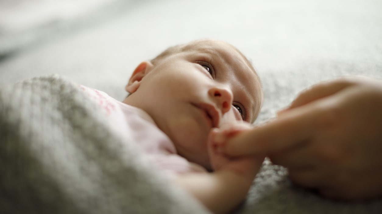A baby is laying on a blanket with a finger on it.