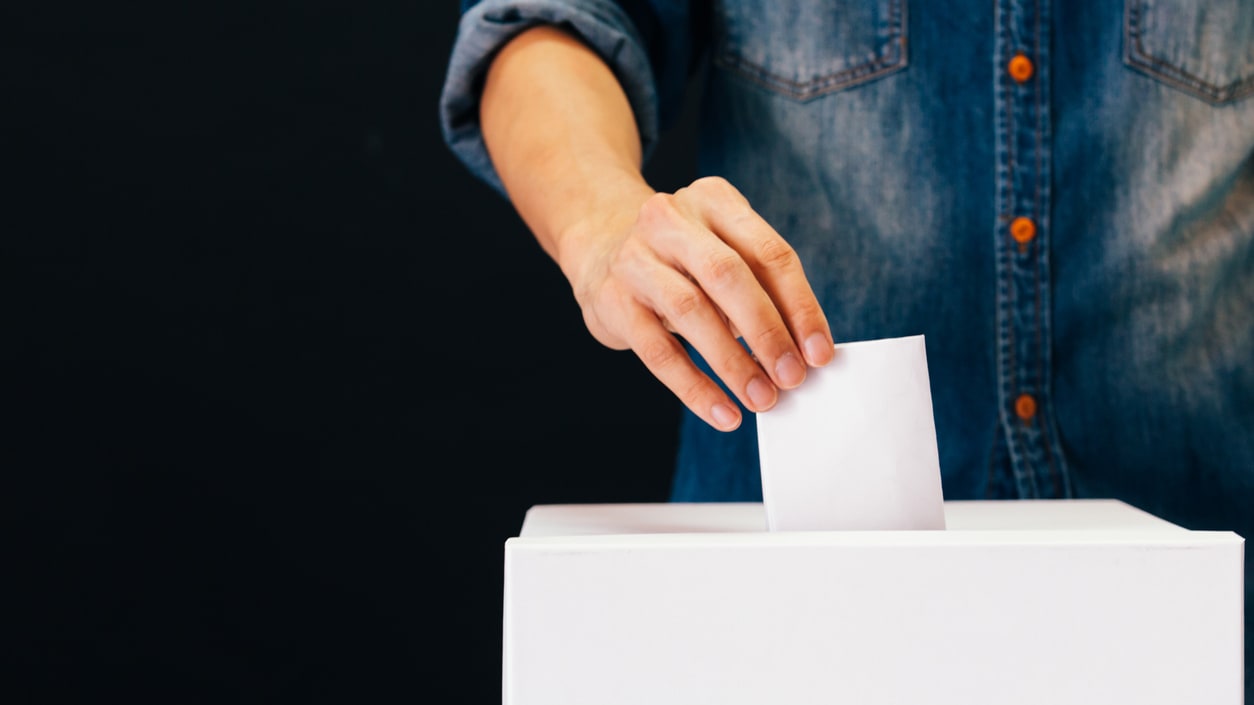 A man is putting a paper into a voting box.