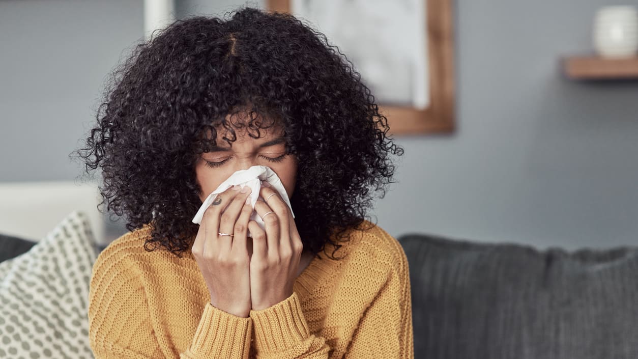 A woman blowing her nose while sitting on a couch.