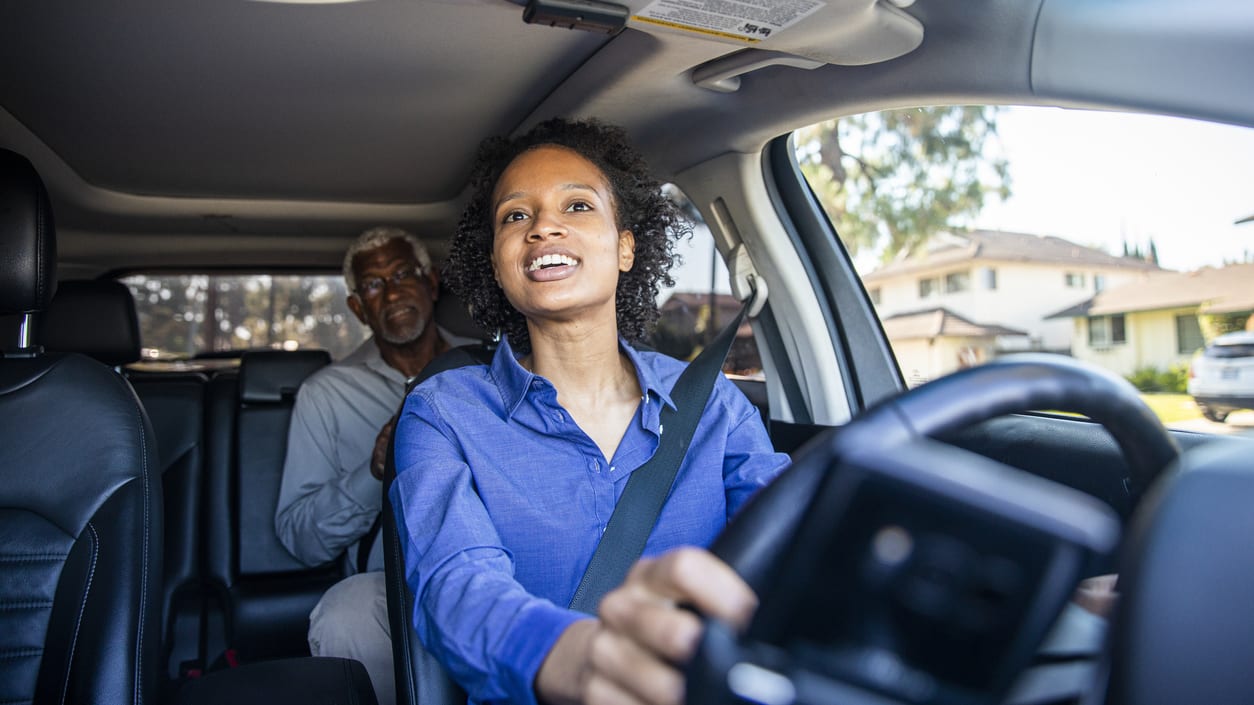 A woman driving a car with an older man in the driver's seat.