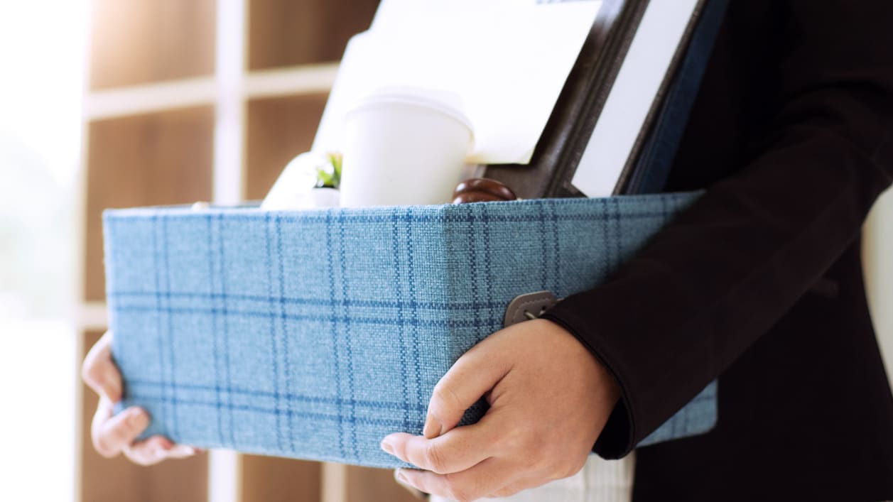 A woman is holding a blue box full of office supplies.