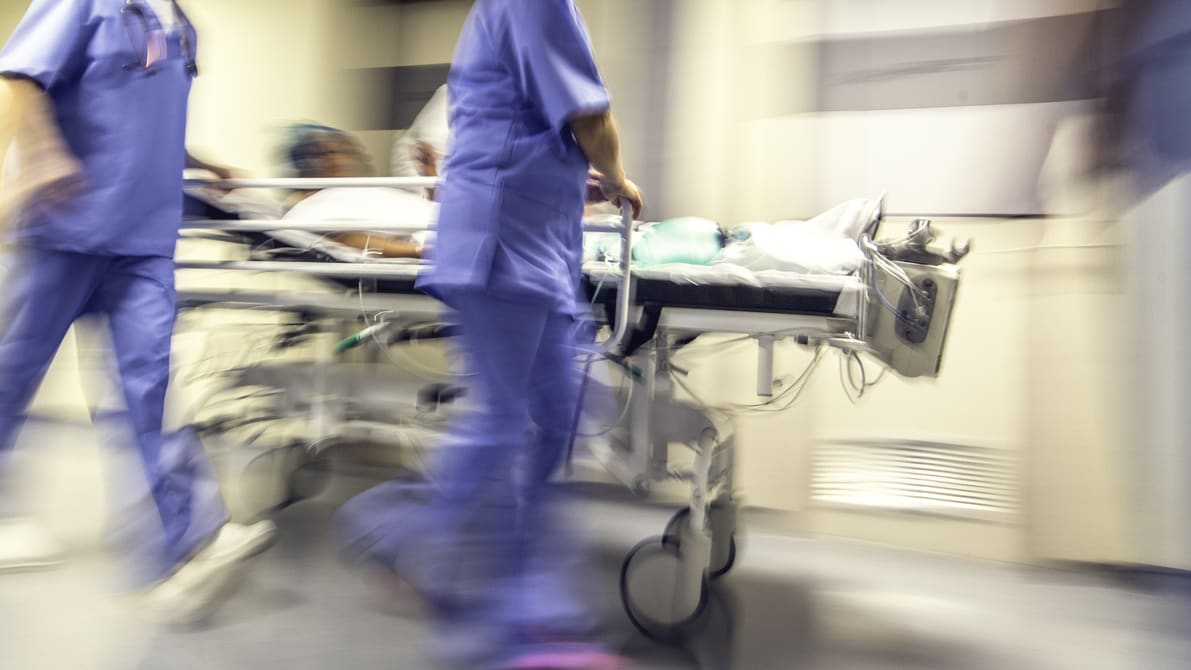 A blurry image of a group of hospital workers pushing a patient on a stretcher.